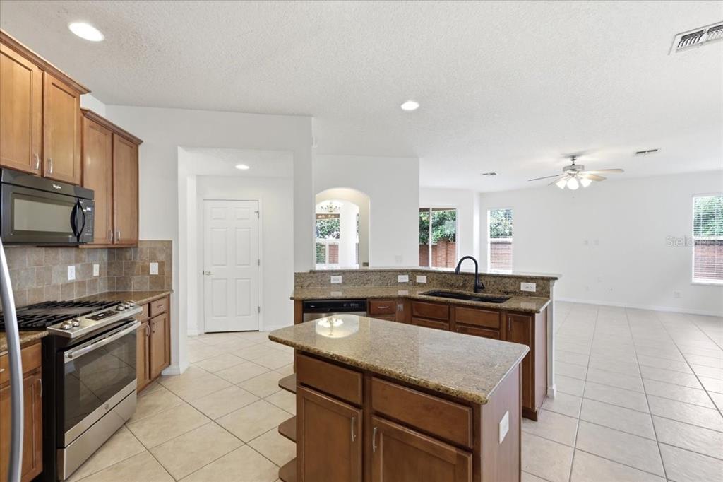 A kitchen with wood cabinets, granite countertops, and an island, opening to a living area — 11854 VIA LUCERNA CIRCLE, WINDERMERE, FL