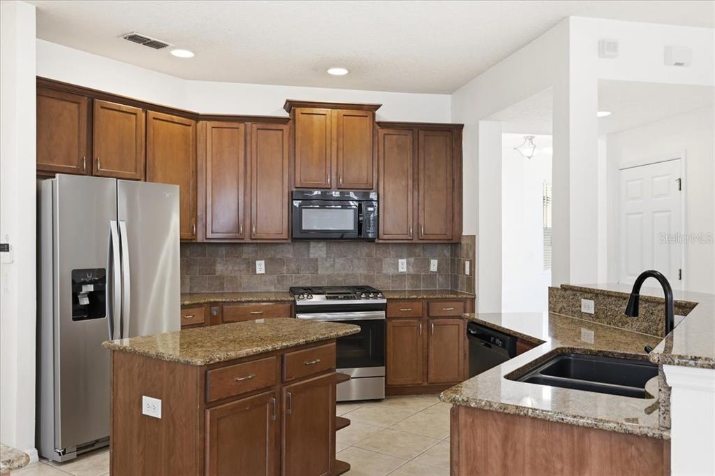 A kitchen features brown wooden cabinets, granite countertops, stainless steel appliances, and a central island — 11854 VIA LUCERNA CIRCLE, WINDERMERE, FL