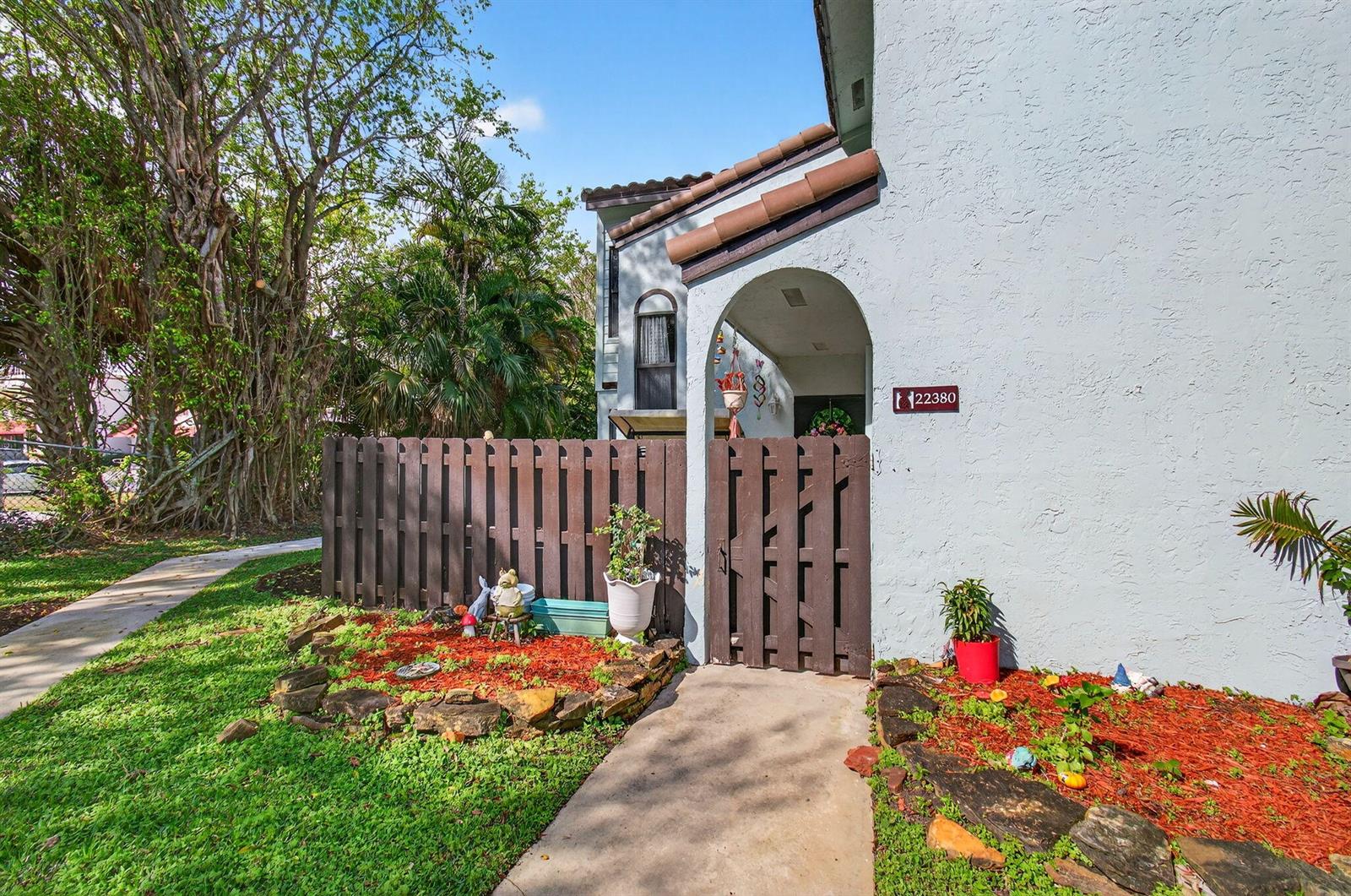 A light blue house exterior features a brown wooden fence and a gated entryway — 22380 Pineapple Walk Drive, Boca Raton FL 33433, BOCA RATON, FL