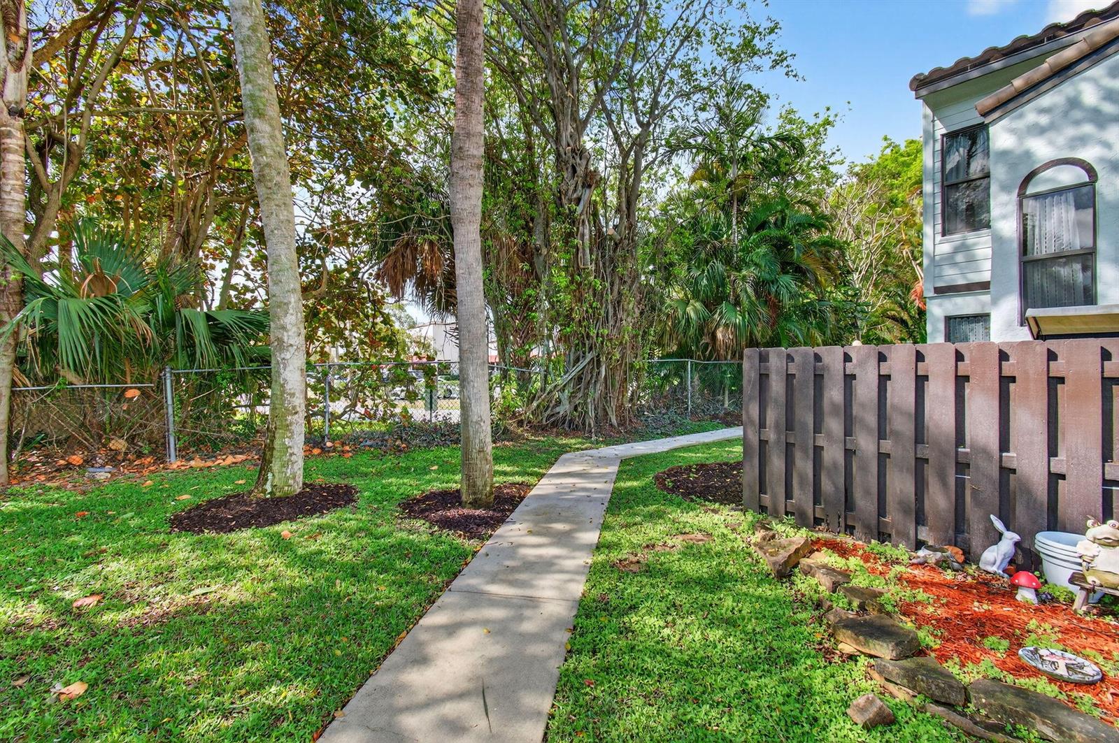 A concrete walkway leads through a grassy yard toward a house with a wooden fence — 22380 Pineapple Walk Drive, Boca Raton FL 33433, BOCA RATON, FL