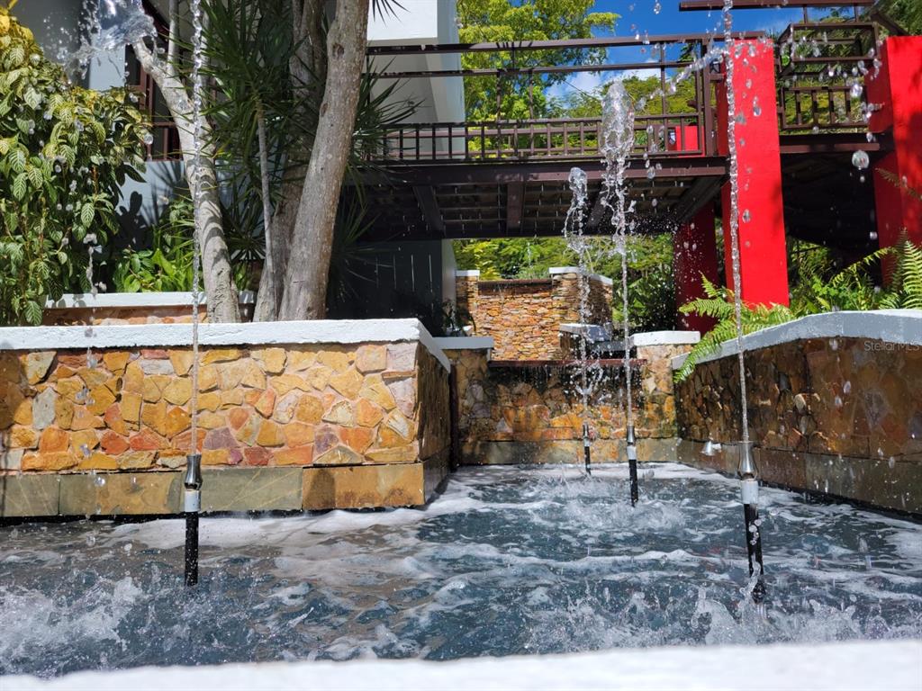 A stone-walled fountain with multiple water jets sits in front of a raised wooden walkway — PR 992 KM3.4 3 ST VILLAS DE LUQUILLO UNIT D18, LUQUILLO, PR
