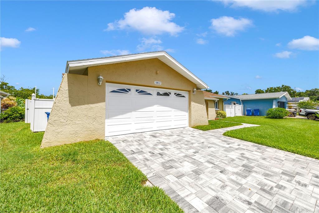 A tan house with a white garage door and a paved driveway under a blue sky — 5812 16TH LANE NE, ST PETERSBURG, FL