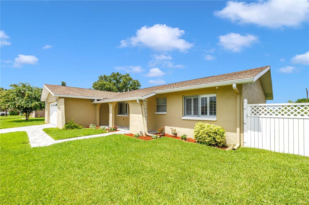 A single-story house with a tan stucco exterior, a shingled roof, and a white fence — 5812 16TH LANE NE, ST PETERSBURG, FL