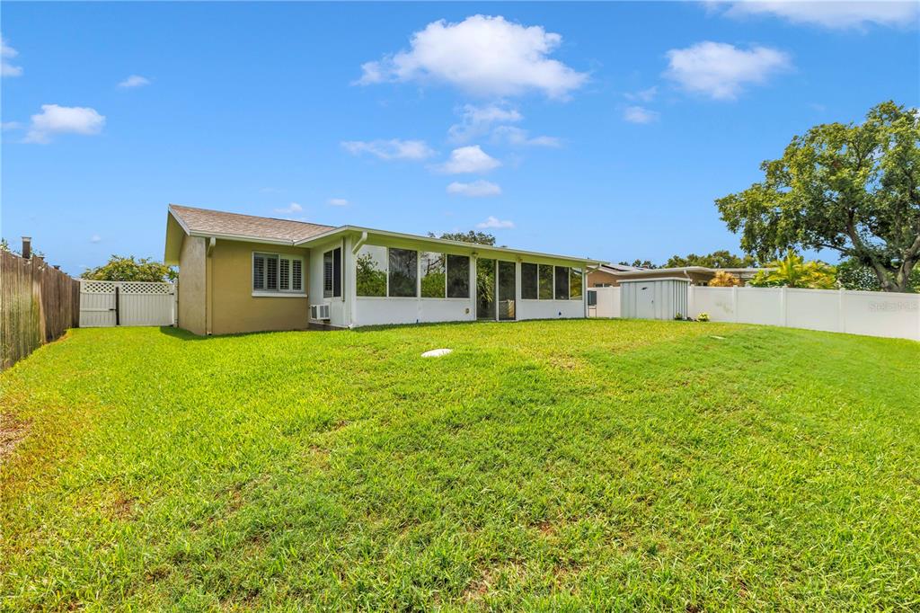 The rear exterior of a house features a large screened-in porch and a grassy yard — 5812 16TH LANE NE, ST PETERSBURG, FL