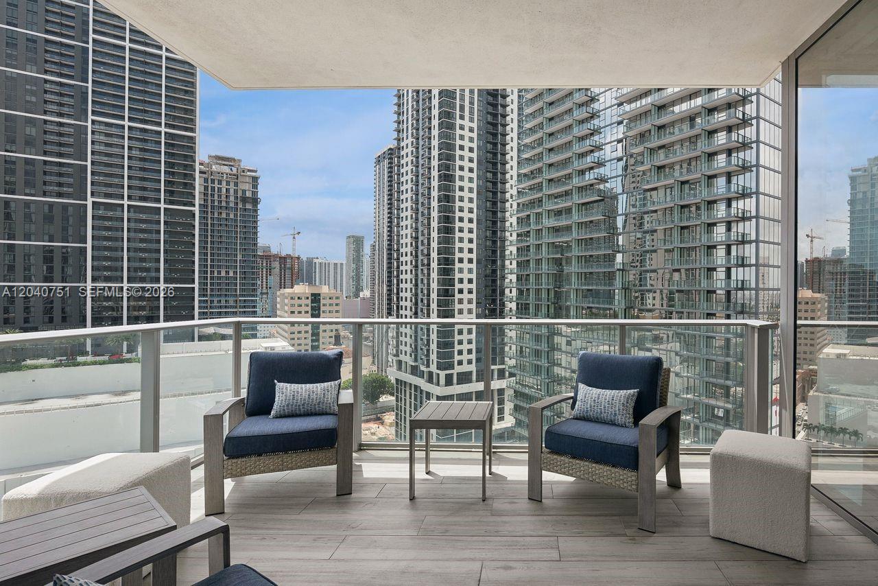 A balcony with two armchairs, a small table, and a view of surrounding city skyscrapers — 851 NE 1st Ave # 1711, Miami FL 33132, MIAMI, FL
