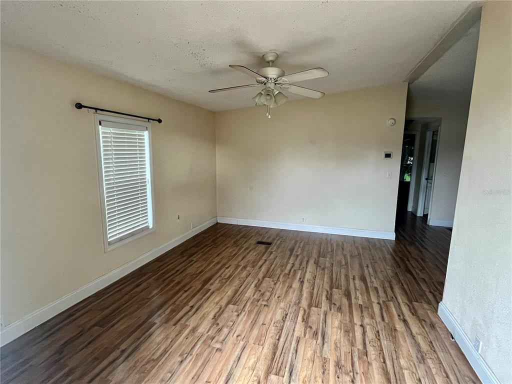 An empty room features wood-look flooring, a ceiling fan, and a window with blinds — 14152 SE 59TH AVENUE, SUMMERFIELD, FL