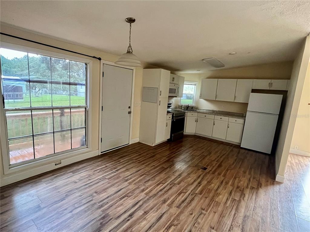 A kitchen with white cabinets, wood-look flooring, and a large window overlooking a backyard — 14152 SE 59TH AVENUE, SUMMERFIELD, FL