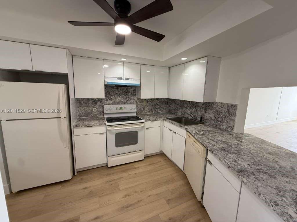 A kitchen features white cabinets, granite countertops, stainless steel appliances, and light wood flooring — 1750 NE 191st St # 2, Miami FL 33179, MIAMI, FL