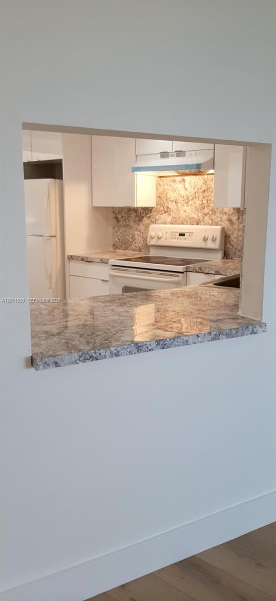A kitchen with white cabinets and a stone countertop is viewed through a wall cutout — 1750 NE 191st St # 2, Miami FL 33179, MIAMI, FL
