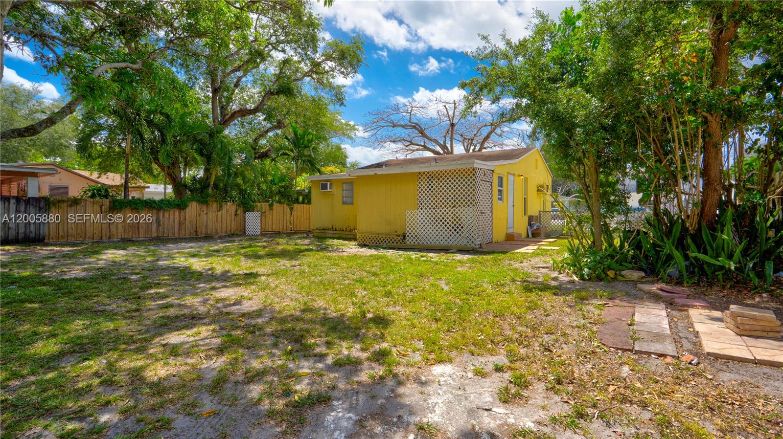 A yellow house with a lattice-enclosed porch sits in a grassy backyard with trees — 1085 NE 128th St, North Miami FL 33161, NORTH MIAMI, FL