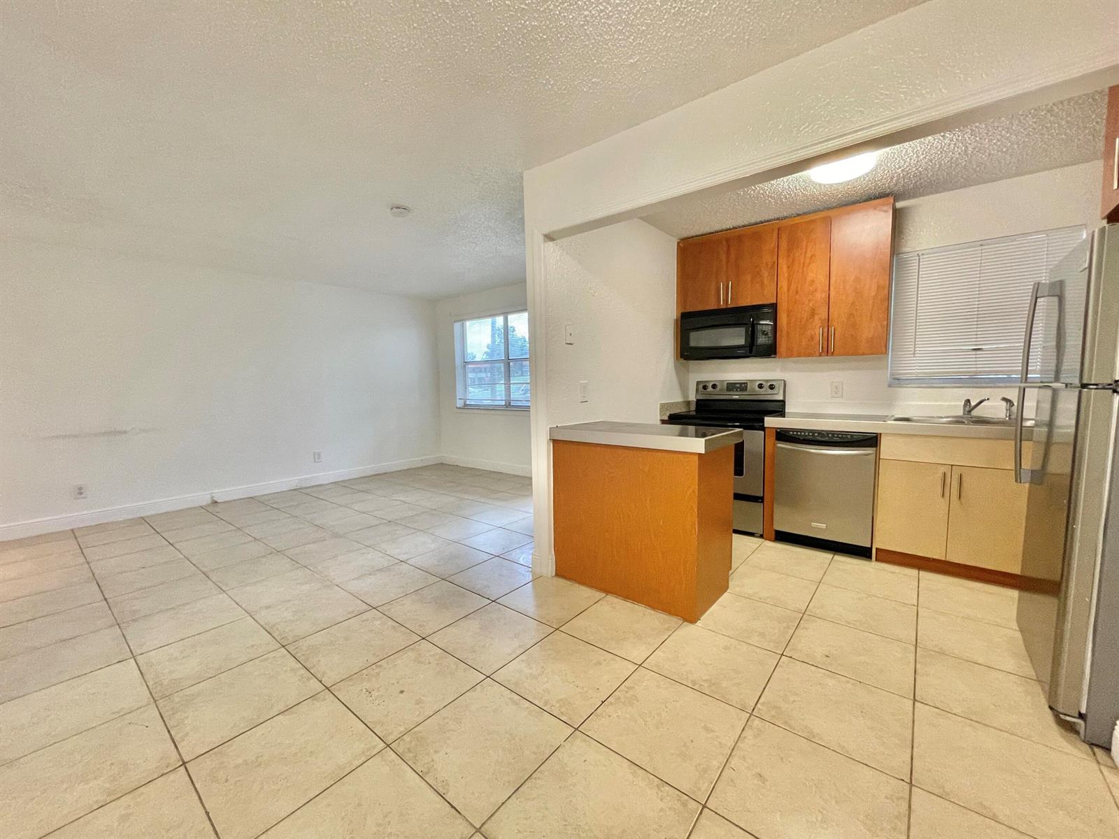 An open-concept kitchen with wood cabinets and stainless steel appliances overlooks a tiled living area — 400 NW 65th Avenue # 114, Margate FL 33063, MARGATE, FL