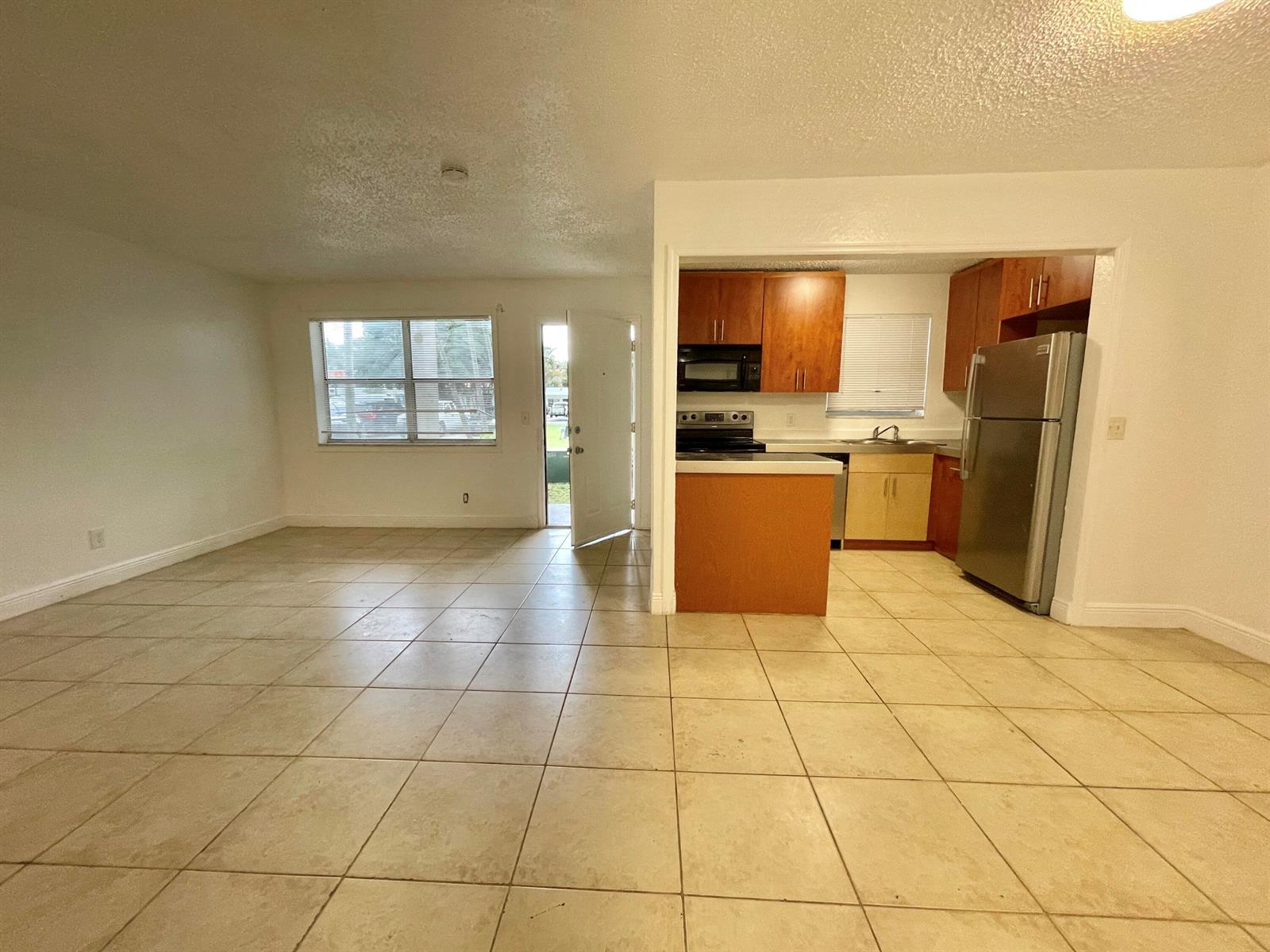 An open-concept living area with tile flooring leads into a kitchen with wood cabinets — 400 NW 65th Avenue # 114, Margate FL 33063, MARGATE, FL