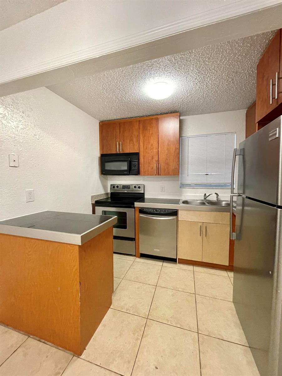 A kitchen features stainless steel appliances, wood cabinets, a small island, and tile flooring — 400 NW 65th Avenue # 114, Margate FL 33063, MARGATE, FL