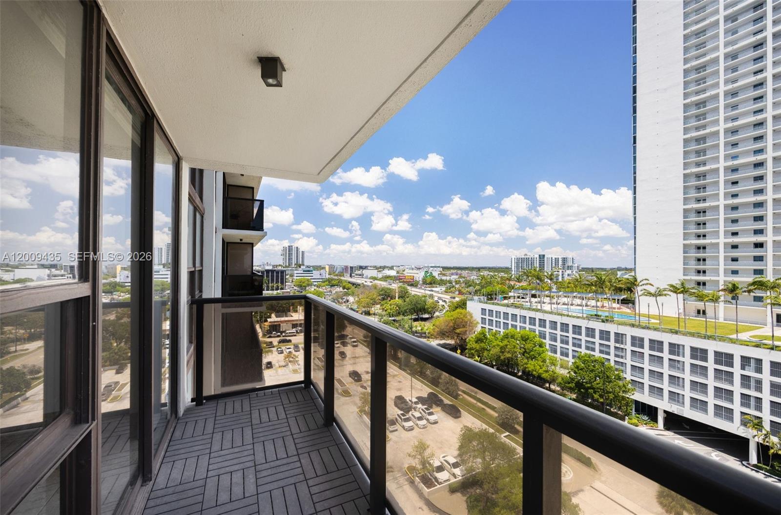 A balcony with dark tiled flooring overlooks a parking lot and surrounding city buildings — 600 NE 36th St # 1109, Miami FL 33137, MIAMI, FL