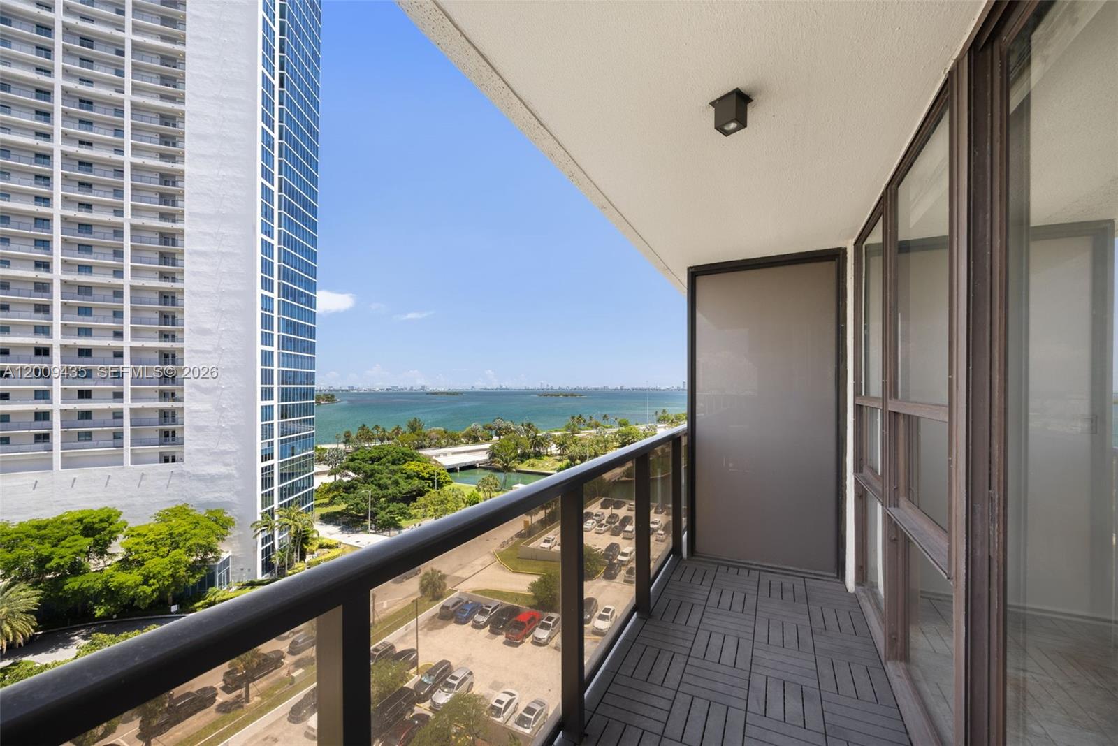A balcony with dark tiled flooring overlooks a parking lot, green space, and the ocean — 600 NE 36th St # 1109, Miami FL 33137, MIAMI, FL