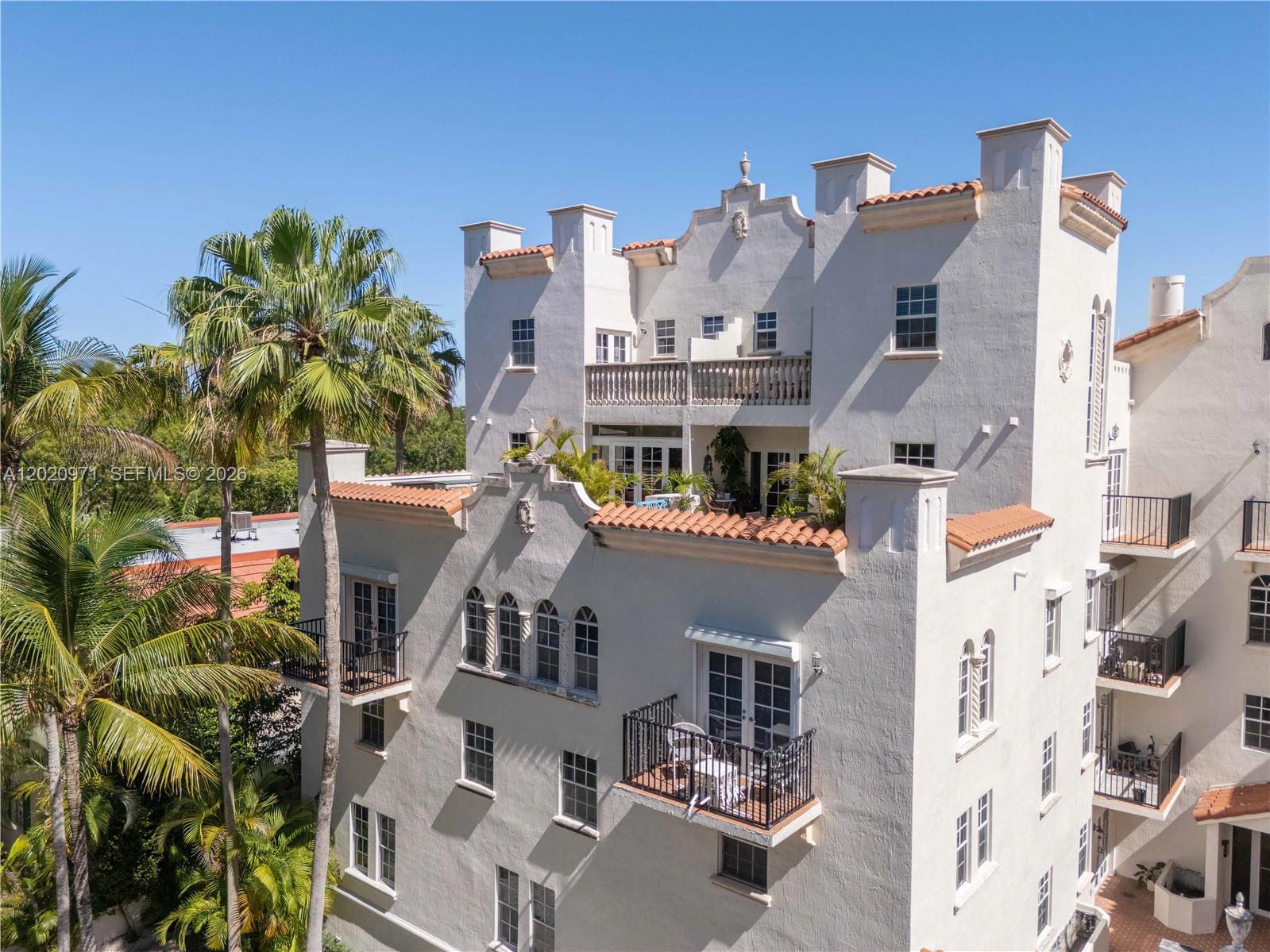 An exterior view of a multi-story Mediterranean-style building with balconies, palm trees, and tiled roofs — 323 Navarre Ave # 403, Coral Gables FL 33134, CORAL GABLES, FL