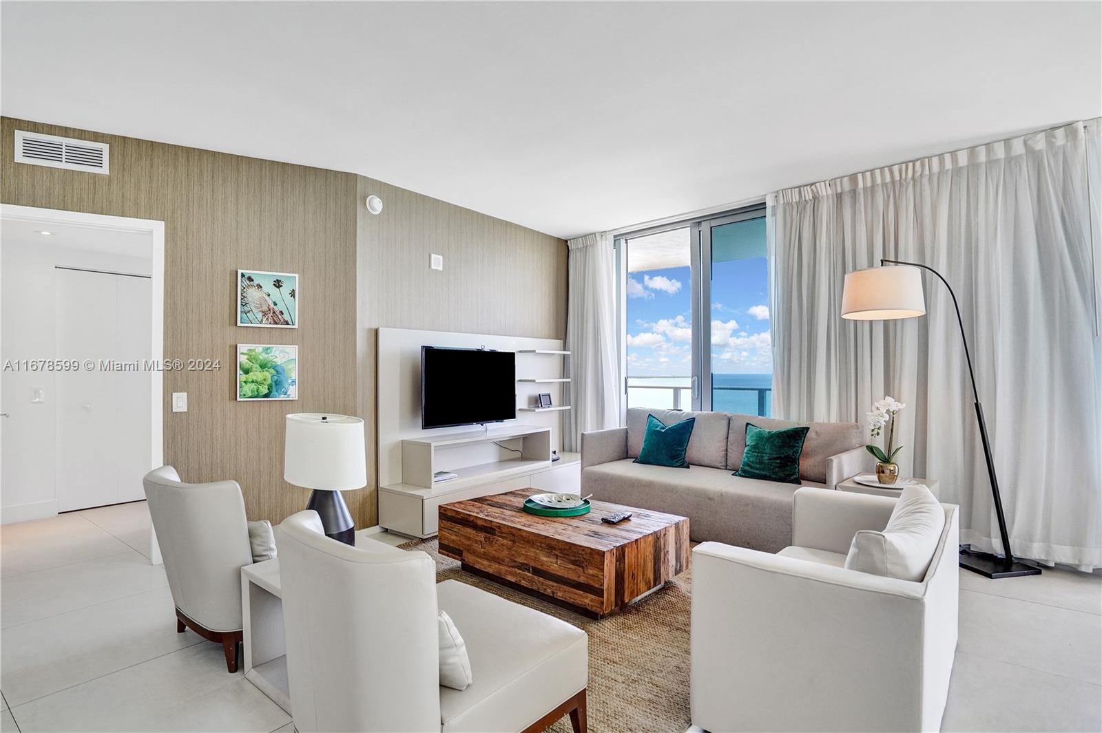 A modern living room features a wooden coffee table, white armchairs, and a balcony view — 4111 S Ocean Dr # 1201, Hollywood FL 33019, HOLLYWOOD, FL