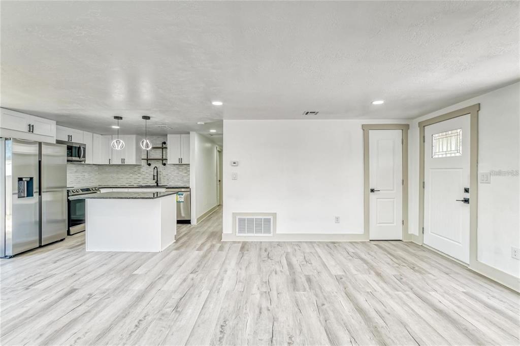 A bright kitchen with white cabinets and an island opens into a living area — 1300 MELONWOOD AVENUE, CLEARWATER, FL