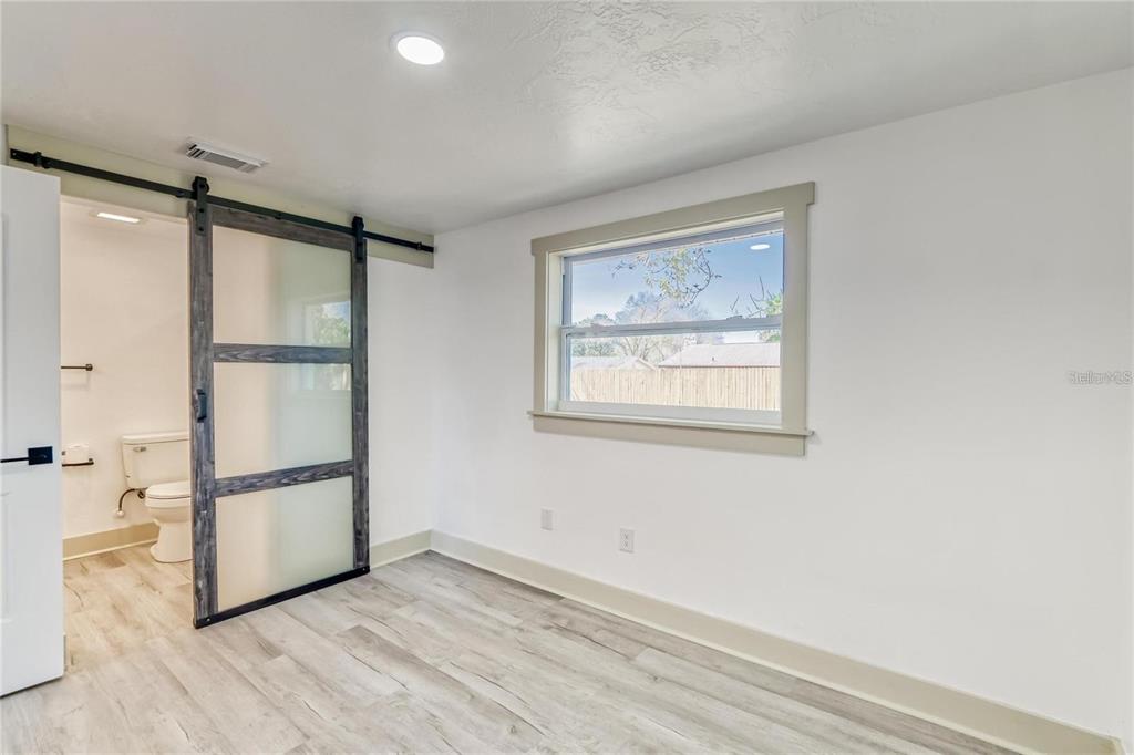 A room with light wood-look flooring, a window, and a sliding barn door to a bathroom — 1300 MELONWOOD AVENUE, CLEARWATER, FL