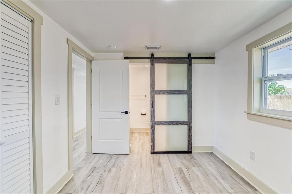 A room with light wood-look flooring, a white door, and a sliding frosted glass barn door — 1300 MELONWOOD AVENUE, CLEARWATER, FL