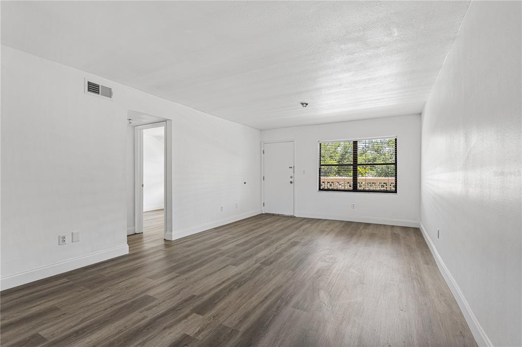 An empty living room with white walls, wood-look flooring, a window, and a doorway — 5080 LOCUST STREET NE UNIT 322, ST PETERSBURG, FL