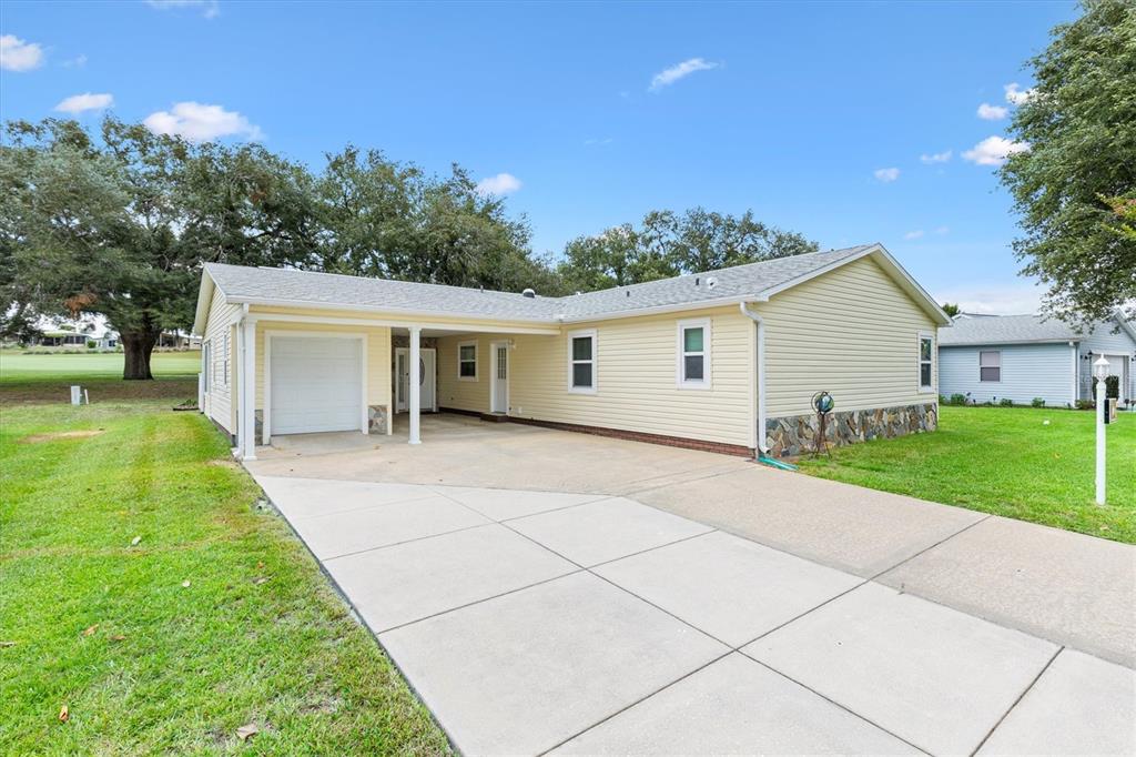 A light yellow single-story house with a carport, concrete driveway, and stone foundation trim — 723 HEATHROW AVENUE, LADY LAKE, FL