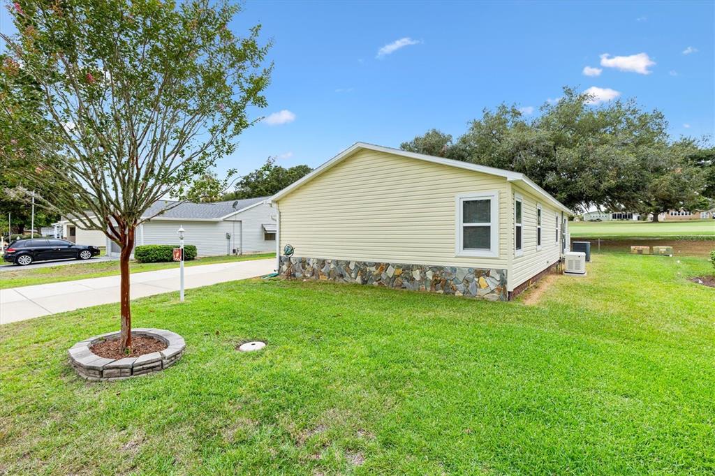 A side view of a light yellow mobile home with a stone-patterned base — 723 HEATHROW AVENUE, LADY LAKE, FL