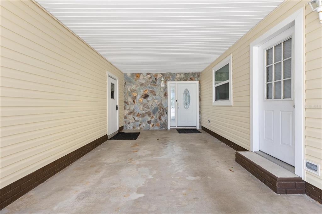 A covered carport with light yellow siding, a stone accent wall, and two white doors — 723 HEATHROW AVENUE, LADY LAKE, FL