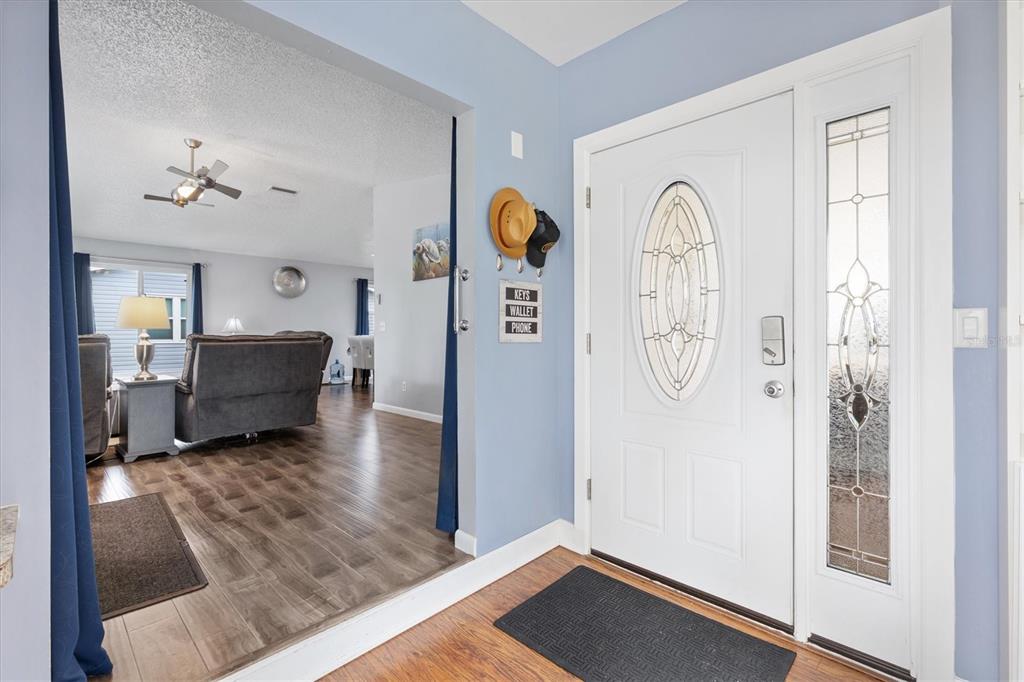 An entryway with a white front door, wood-look flooring, and a view into the living room — 723 HEATHROW AVENUE, LADY LAKE, FL