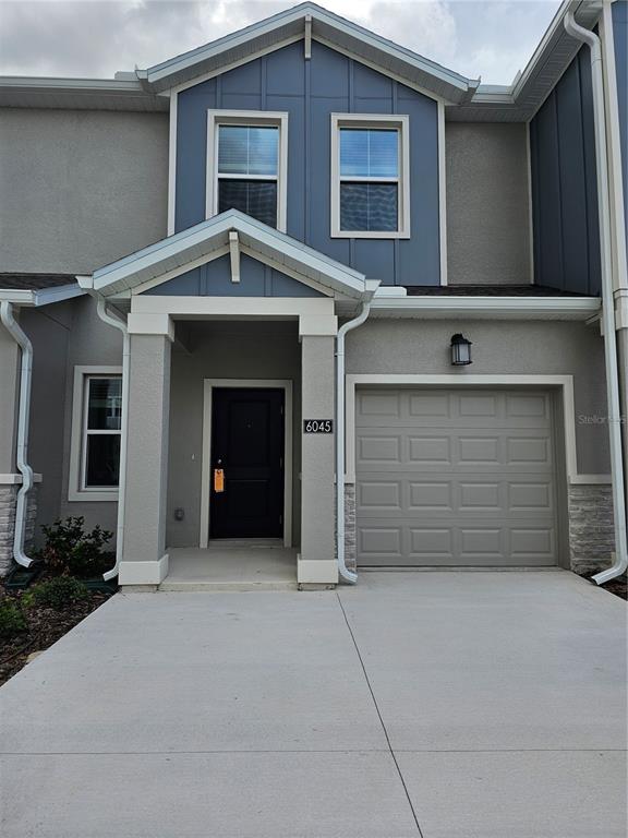 A two-story townhouse exterior features a gray garage, a covered entryway, and blue siding — 6045 ZEN WAY UNIT 6045, CLERMONT, FL