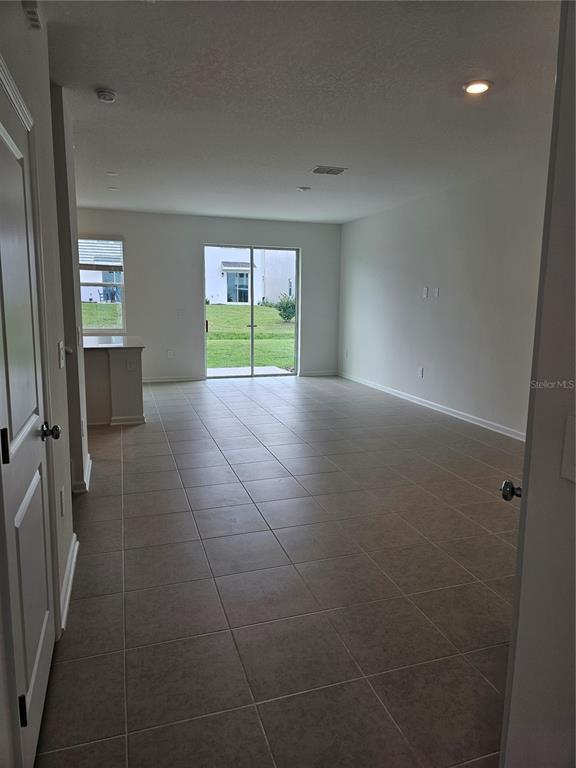 An open-concept living area features light-colored tile flooring, a kitchen island, and sliding glass doors — 6045 ZEN WAY UNIT 6045, CLERMONT, FL