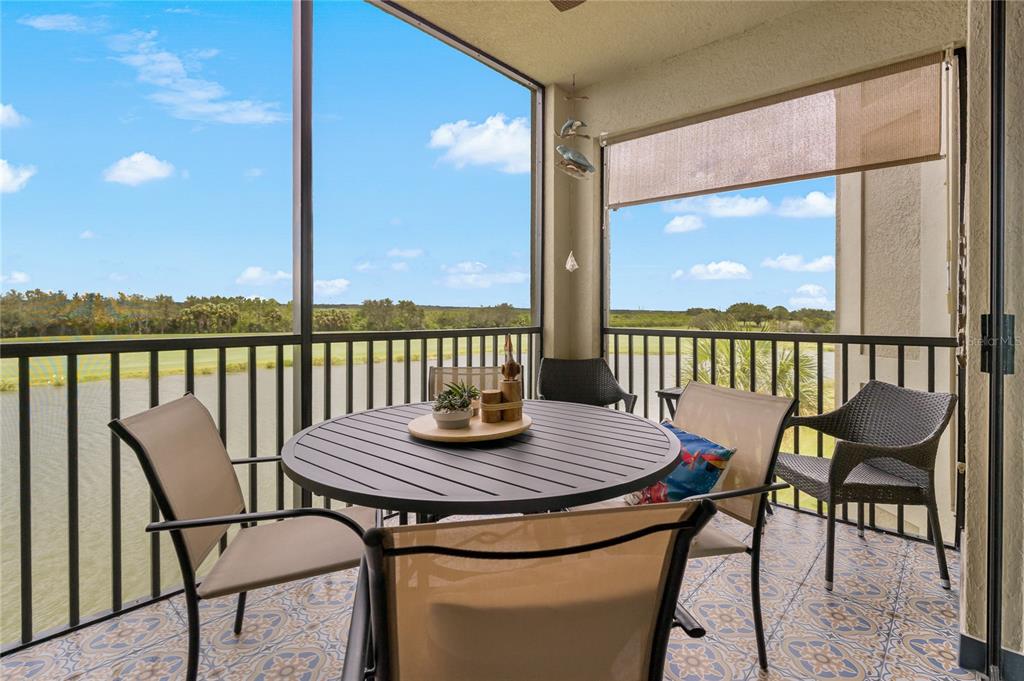 A screened-in balcony features a round table, chairs, patterned tile flooring, and a water view — 7015 RIVER HAMMOCK DRIVE UNIT 306, BRADENTON, FL