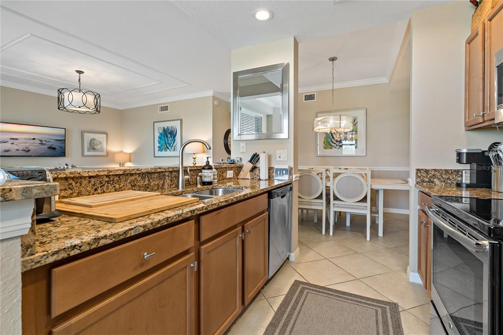 A kitchen with granite countertops, wood cabinets, and stainless steel appliances overlooks a dining area — 7015 RIVER HAMMOCK DRIVE UNIT 306, BRADENTON, FL