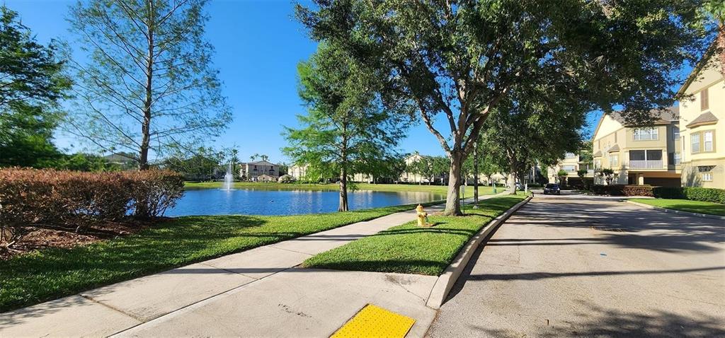 A paved walkway runs alongside a pond with a fountain near apartment buildings and trees — 2262 GRAND CENTRAL PARKWAY UNIT 2, ORLANDO, FL