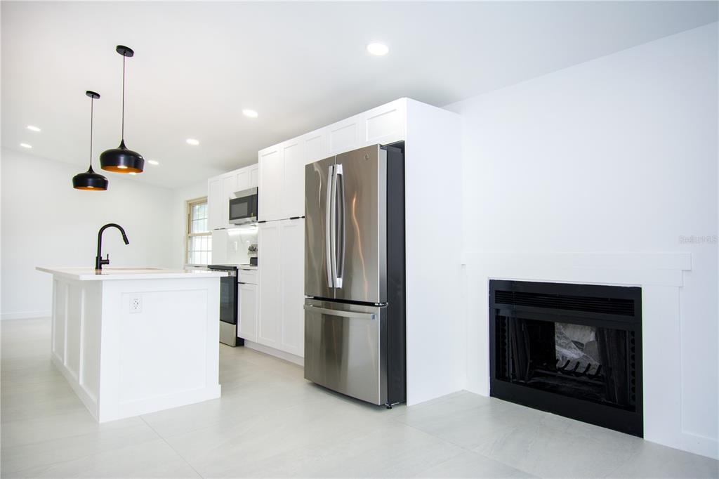 A modern kitchen features white cabinetry, stainless steel appliances, a center island, and a fireplace — 9409 LONSDALE COURT, TAMPA, FL