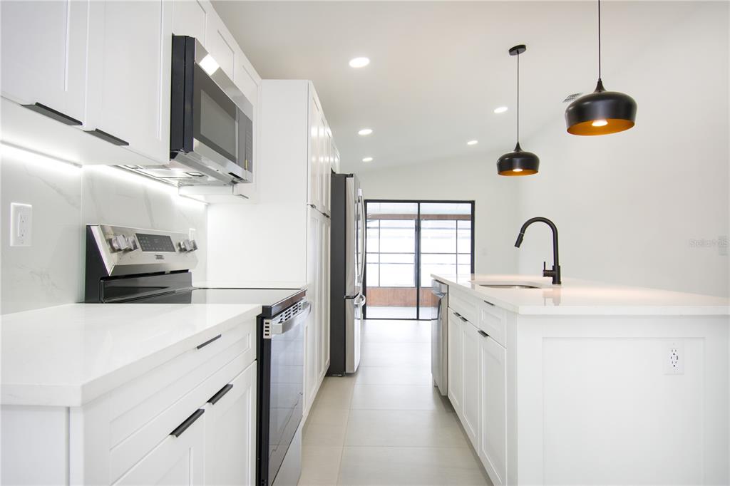 A modern white kitchen features stainless steel appliances, a center island, and two pendant lights — 9409 LONSDALE COURT, TAMPA, FL