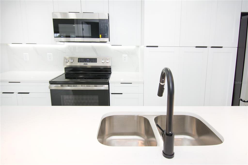 A modern kitchen features white cabinets, stainless steel appliances, a quartz island, and a black faucet — 9409 LONSDALE COURT, TAMPA, FL