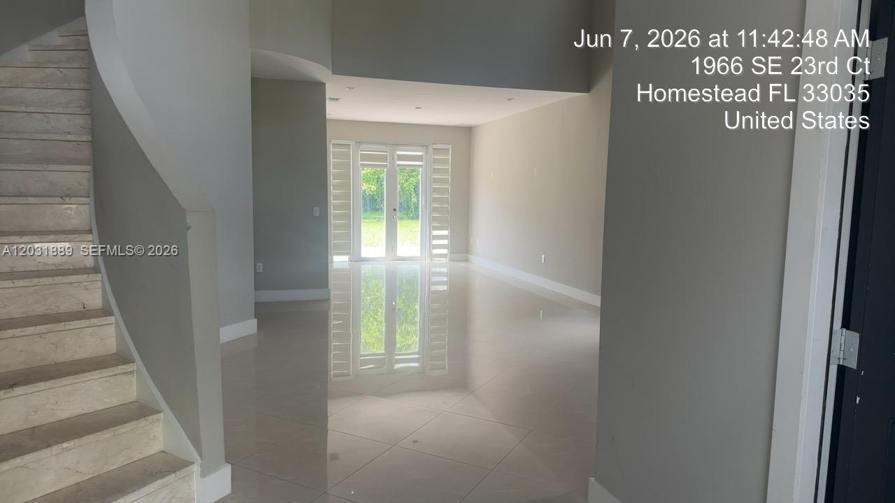 An interior view shows a tiled foyer with a staircase and glass double doors — 1974 SE 23rd Ct, Homestead FL 33035, HOMESTEAD, FL
