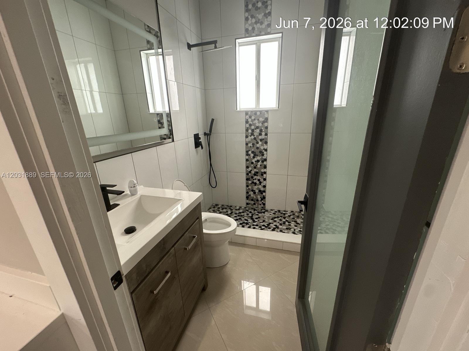 A modern bathroom features a wood vanity, a walk-in shower with pebble flooring, and tile — 1974 SE 23rd Ct, Homestead FL 33035, HOMESTEAD, FL