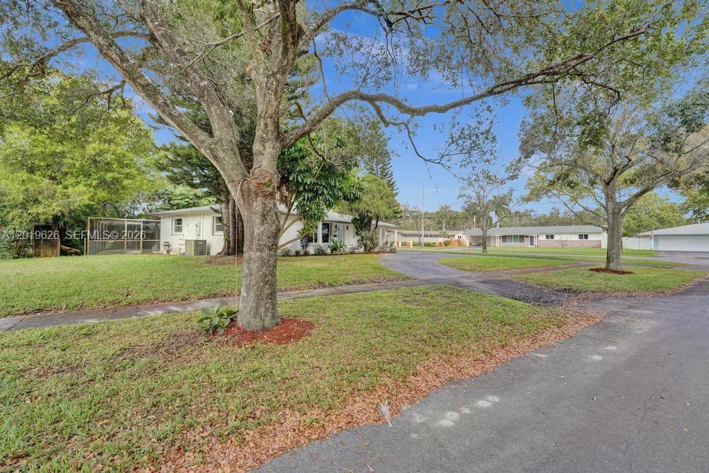 A white single-story house sits on a grassy lot with mature trees and a driveway — 101 SW 53rd Ave, Plantation FL 33317, PLANTATION, FL