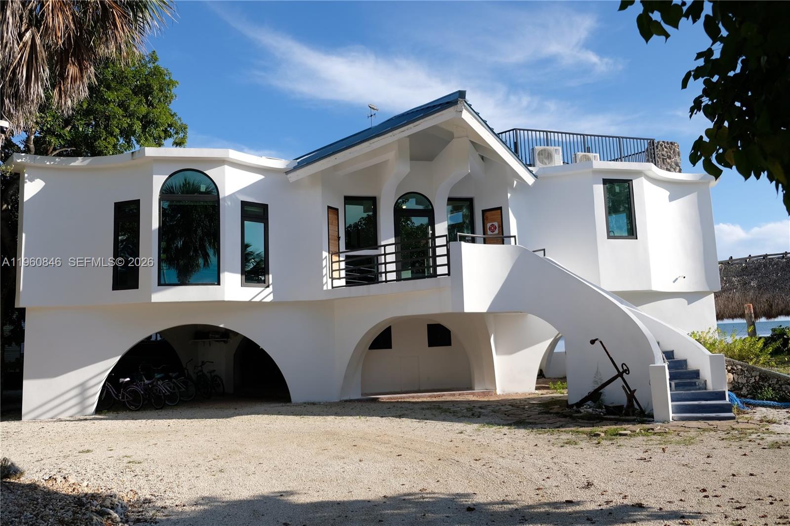 A white, two-story house with arched ground-level openings and an exterior staircase leading to a balcony — 1557 Long Beach Dr, Big Pine FL 33043, BIG PINE, FL