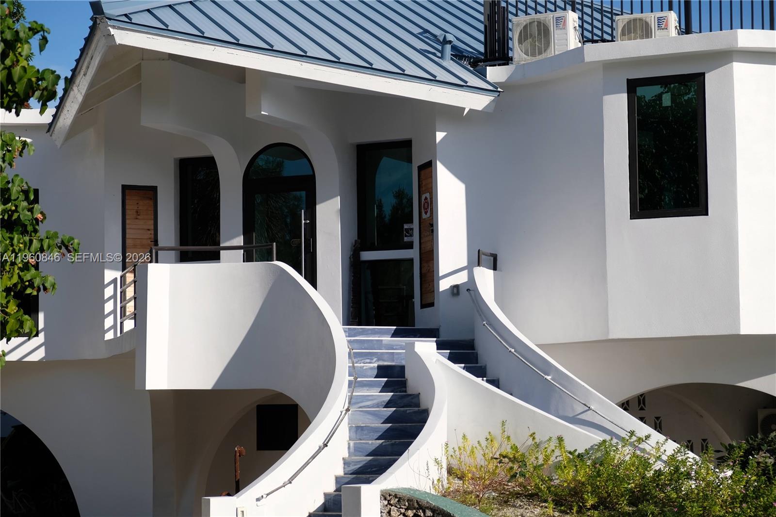 A white building features a curved staircase leading to an elevated entrance with glass doors — 1557 Long Beach Dr, Big Pine FL 33043, BIG PINE, FL