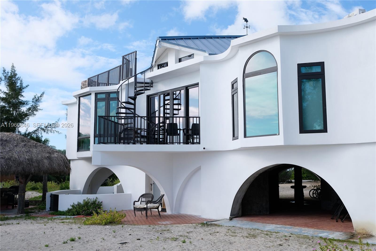 A white two-story house features arched ground-level openings, a balcony, and a spiral staircase — 1557 Long Beach Dr, Big Pine FL 33043, BIG PINE, FL