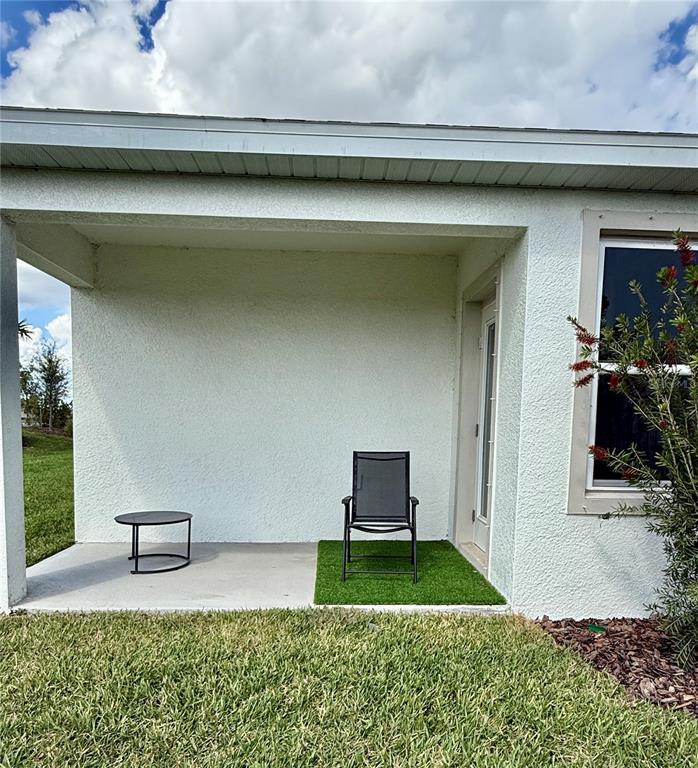 A covered concrete patio features a small table, a single chair, and artificial turf — 3222 BITTERROOT LANE, BRADENTON, FL