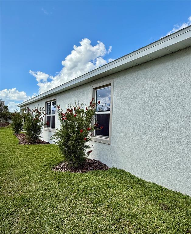 The exterior of a light-colored stucco house features two windows and two flowering bushes — 3222 BITTERROOT LANE, BRADENTON, FL
