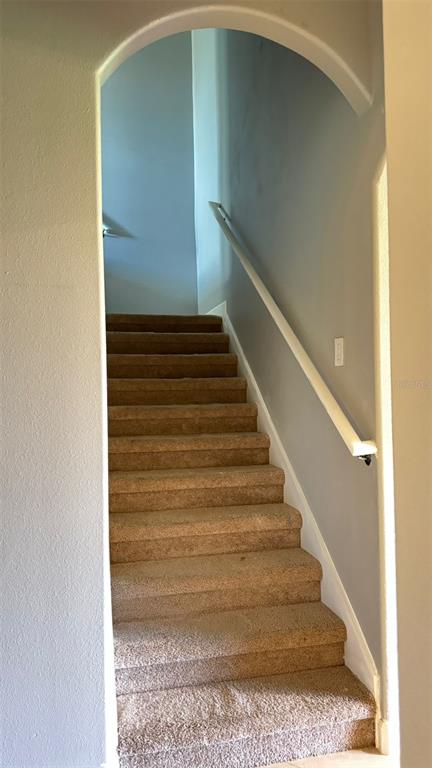 A carpeted staircase with a white handrail leads upward through an arched entryway — 1428 DEUCE CIRCLE, DAVENPORT, FL