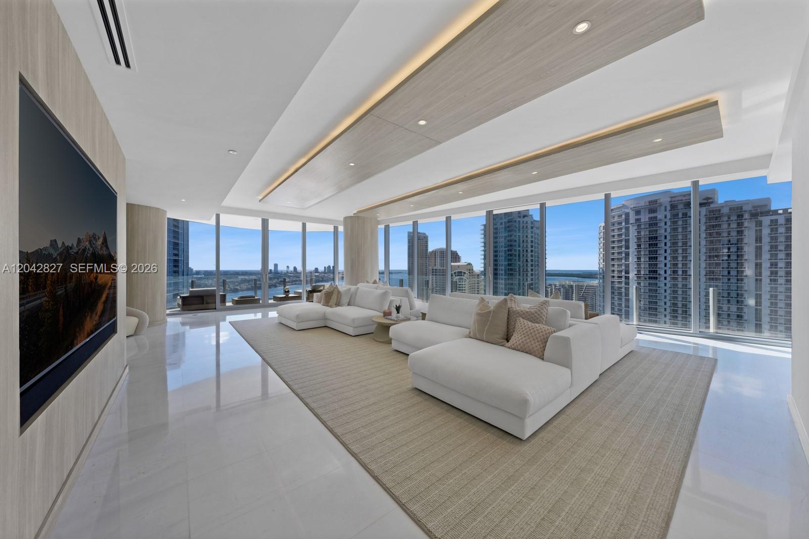 A modern living room features white sectional sofas, a large television, and floor-to-ceiling windows — 300 Biscayne Boulevard Way # 2701, Miami FL 33131, MIAMI, FL