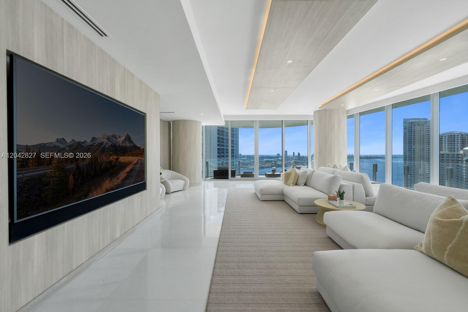 A modern living room features white sofas, a large wall-mounted television, and floor-to-ceiling windows — 300 Biscayne Boulevard Way # 2701, Miami FL 33131, MIAMI, FL