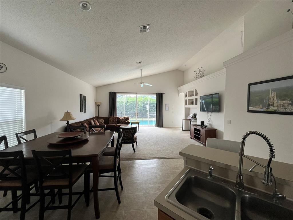 An open-concept living and dining area features tile flooring, a vaulted ceiling, and pool views — 16628 FRESH MEADOW DRIVE, CLERMONT, FL