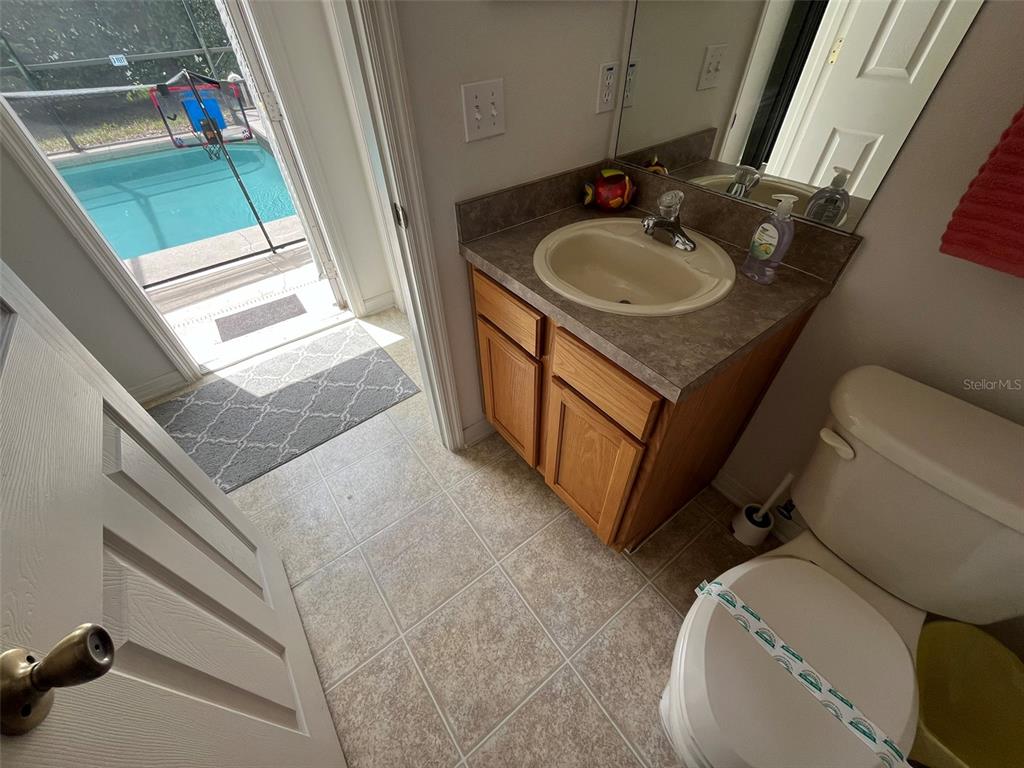 A bathroom with a vanity, toilet, and a glass door leading to a pool area — 16628 FRESH MEADOW DRIVE, CLERMONT, FL